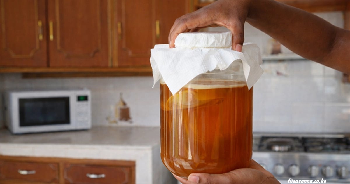 A person holding a glass jar of homemade kombucha with a SCOBY culture