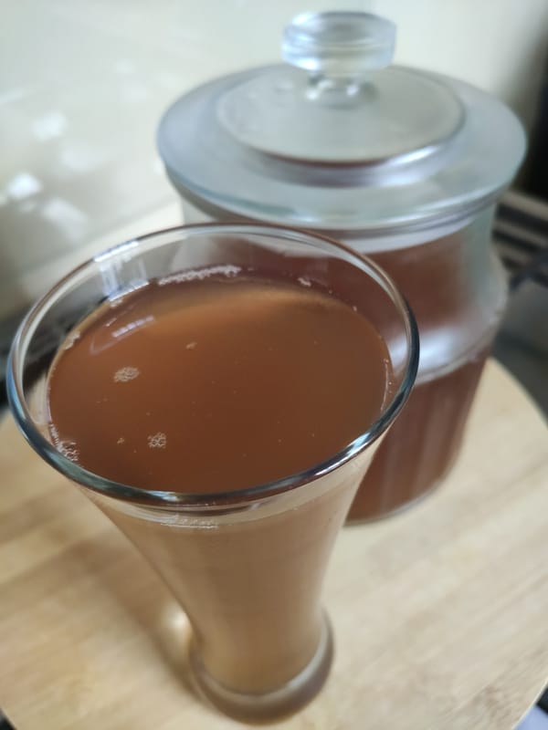 Glass of freshly brewed kombucha with a fermentation jar in the background