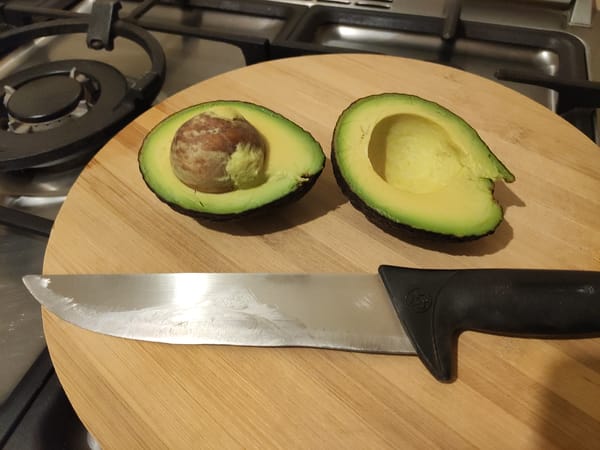 Halved avocado on a wooden board next to a kitchen knife