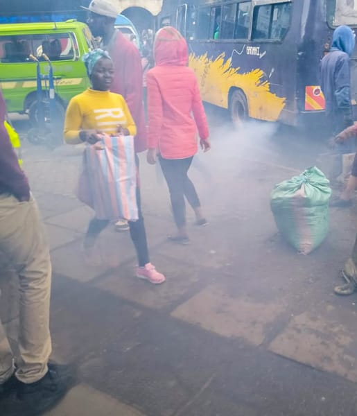 People walking through a busy Nairobi market area with heavy exhaust smoke from matatus and vehicles